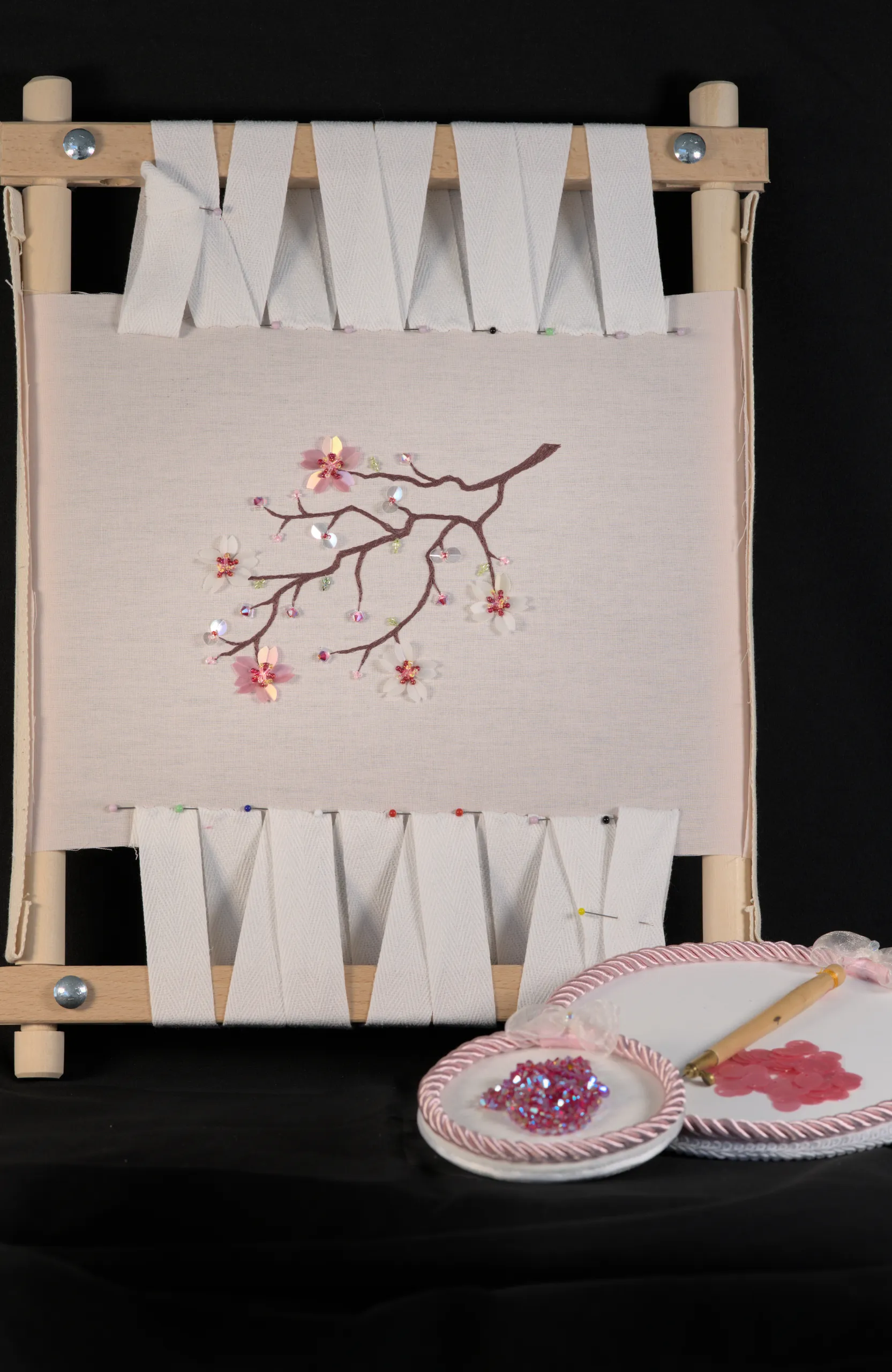 Bastidor de bordado con una rama de sakura y delicadas flores bordadas con abalorios y lentejuelas, que muestra el bordado en tambor y las técnicas de alta costura.