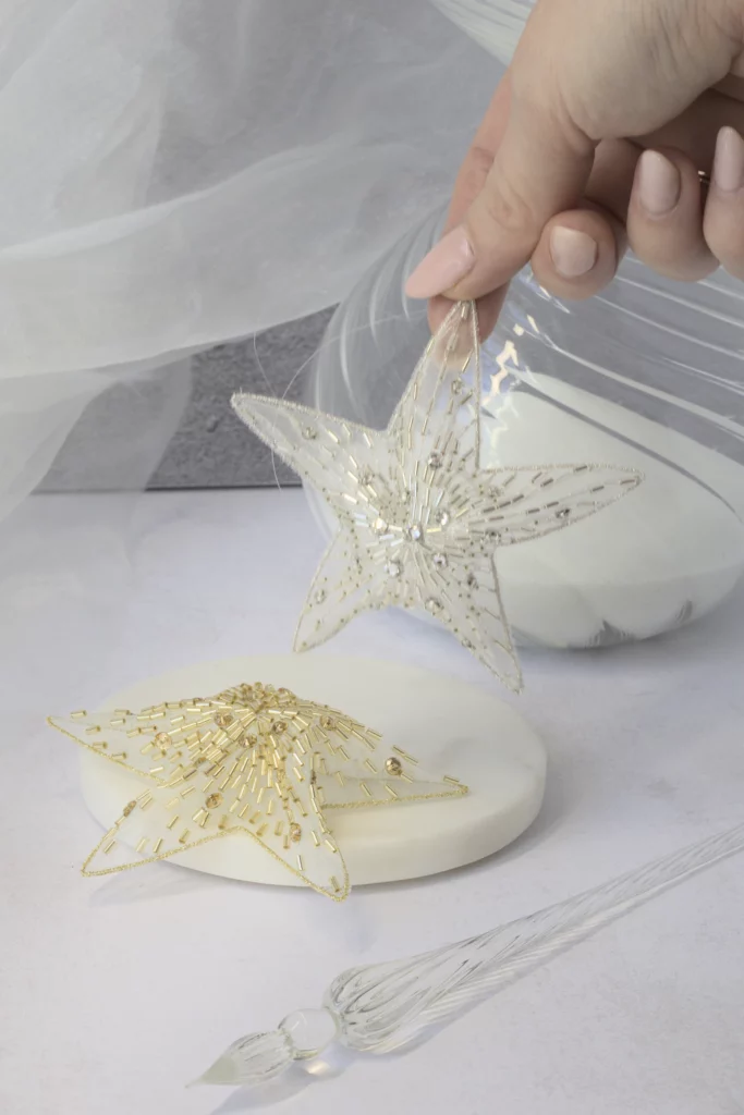 Una estrella de Navidad Polaris bordada a mano en las manos, mostrando sus intrincados pespuntes en 3D y sus brillantes adornos de cristal.