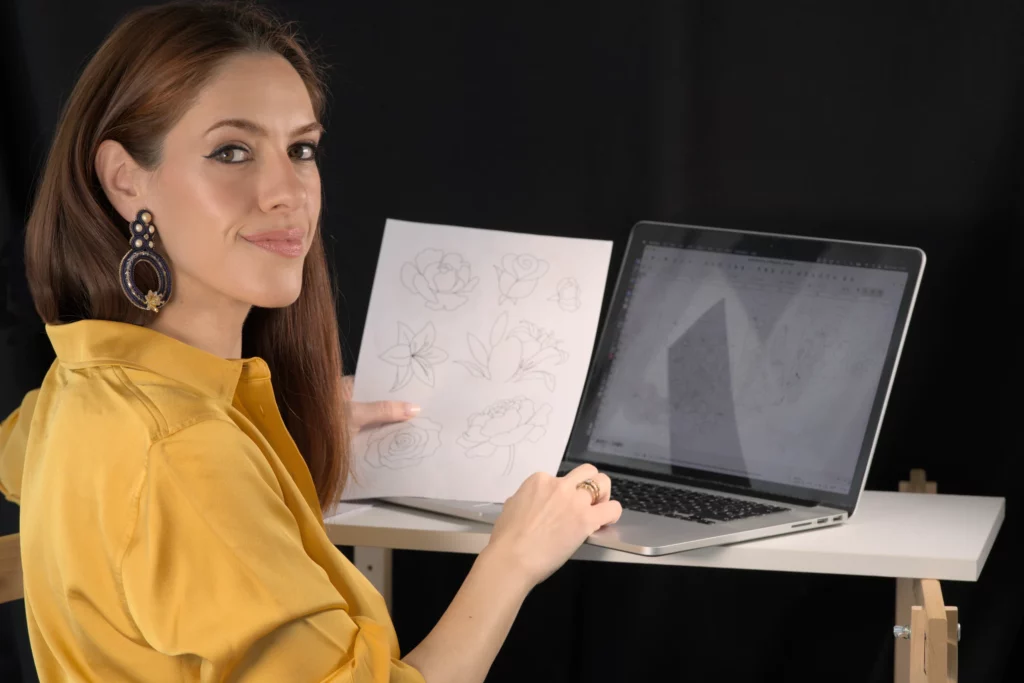 Laura S. Urbina présente un motif de broderie imprimé sur son ordinateur, mettant en valeur son service de conception de broderies numériques personnalisées.
