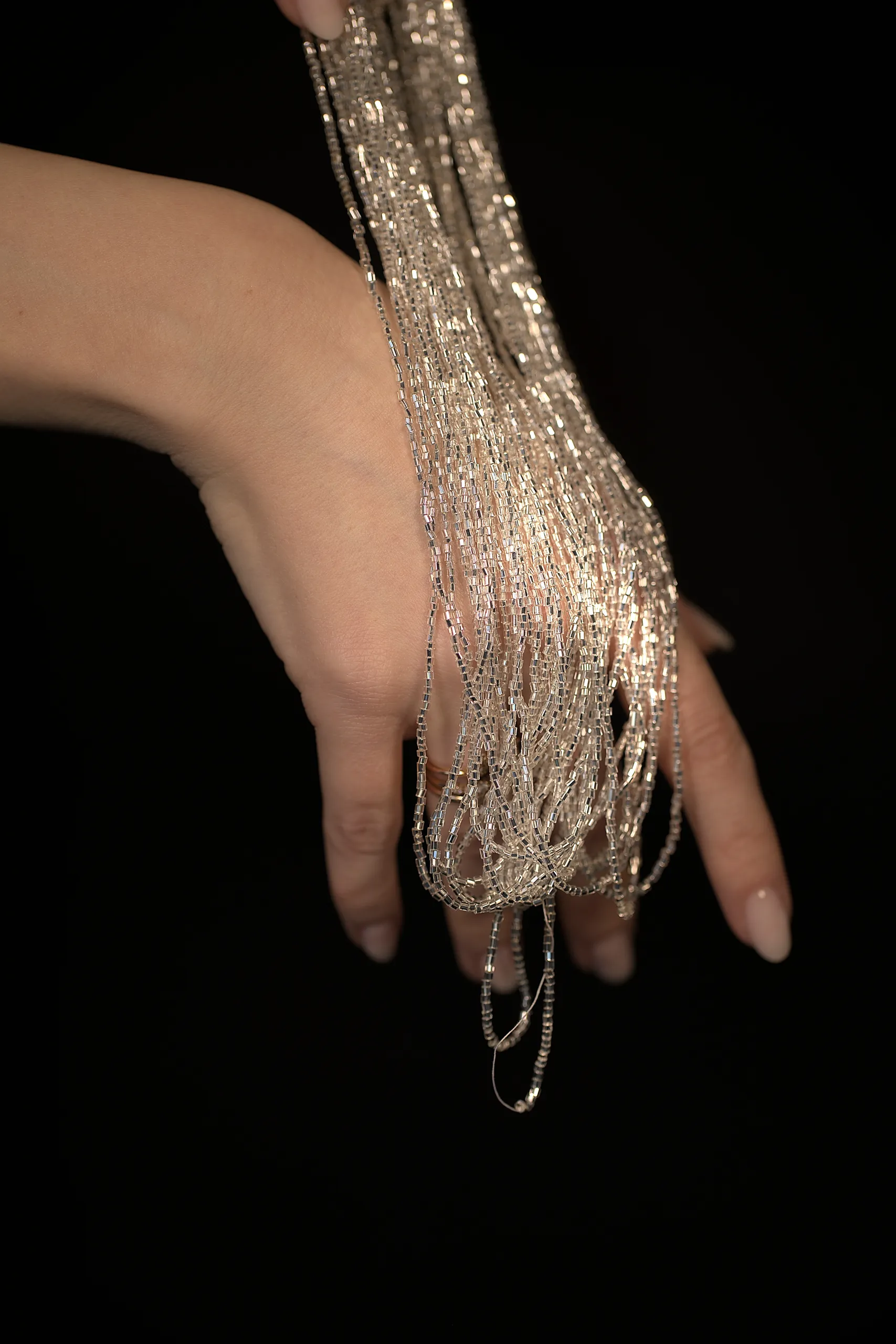 Delicate hand holding shimmering crystal beads in a macro shot, highlighting the elegance of Haute Couture embroidery.