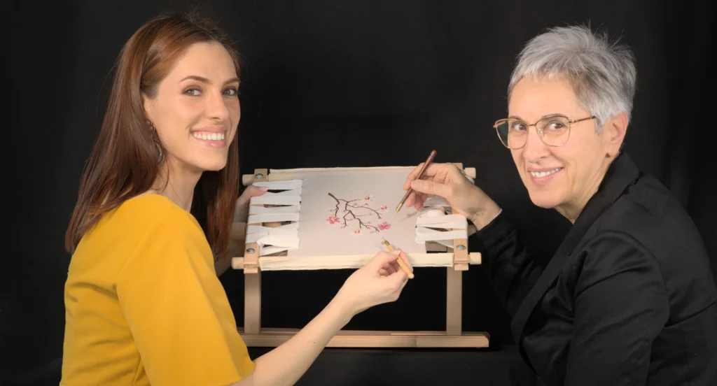 Embroidery instructor Laura S. Urbina demonstrating needle and Luneville hook techniques to a student during a hands-on Haute Couture embroidery workshop.