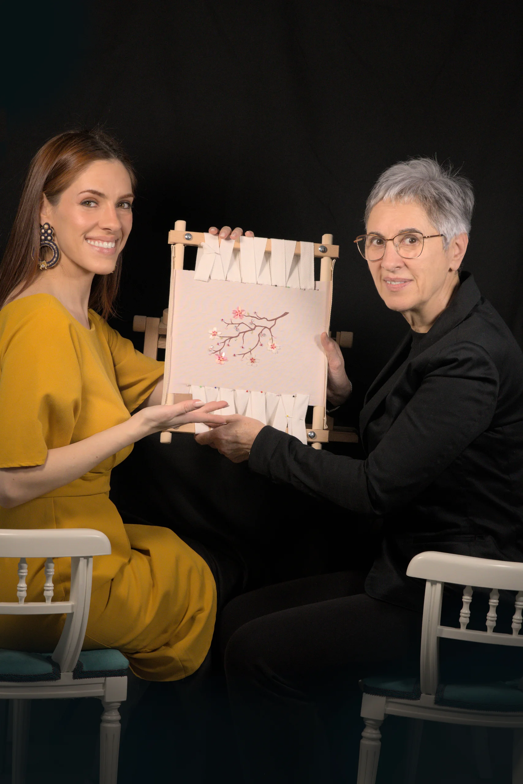 Embroidery instructor Laura S. Urbina guiding a student at a Haute Couture embroidery workshop, both working together on a shared embroidery frame.